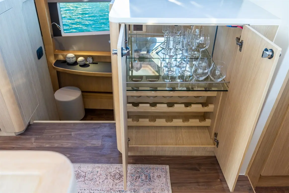 Glassware inside a wooden cabinet on a boat, with modern decor and a glimpse of water through a nearby window.